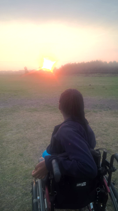 A picture of me from behind with the sunset in front of me and my wheelchair in a wide, open field 