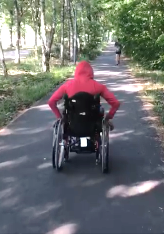 Me from behind in my wheelchair pushing it along a pathway in nature