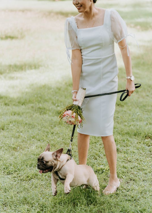 A picture of a woman in a white dress holding back her dog who is pulling at the leash