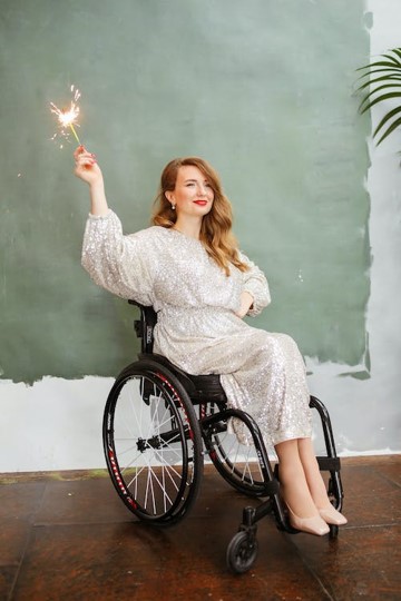 A woman in a wheelchair is waving a sparkler in a beautiful white dress. She is smiling and looks beautiful. 